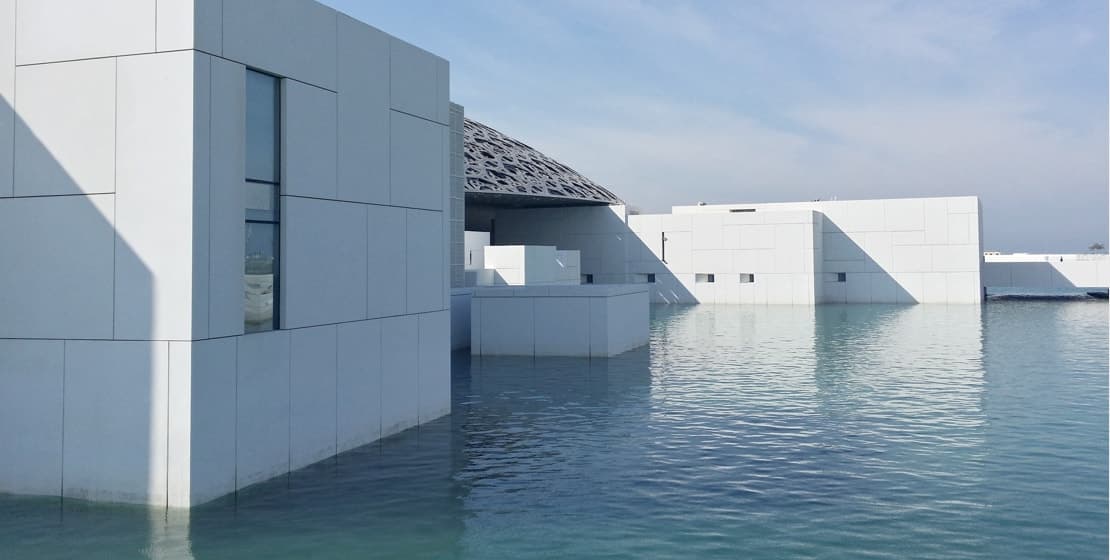 Modern white geometric buildings over calm blue water.